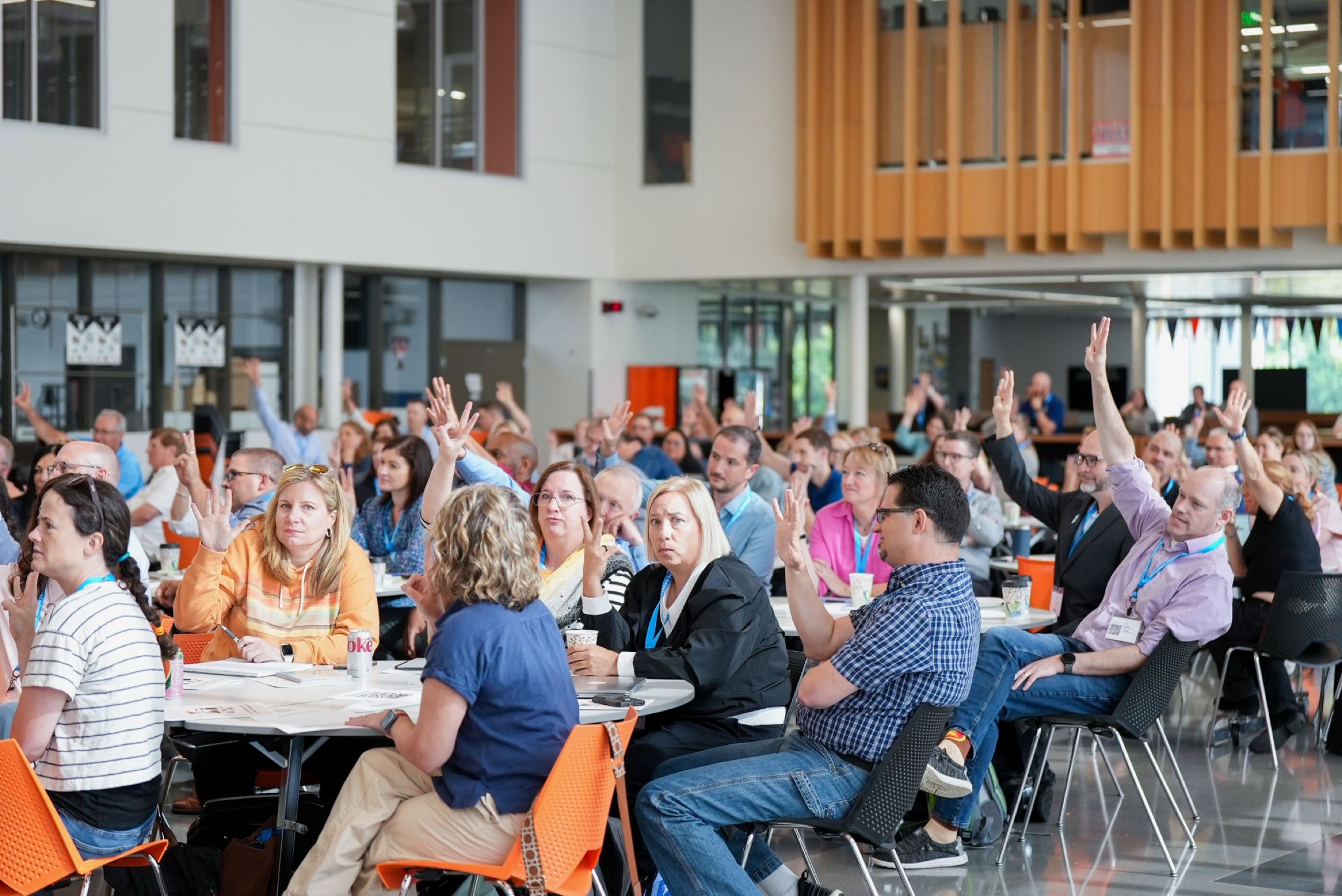 A room full of participants at round tables with their hands raised.