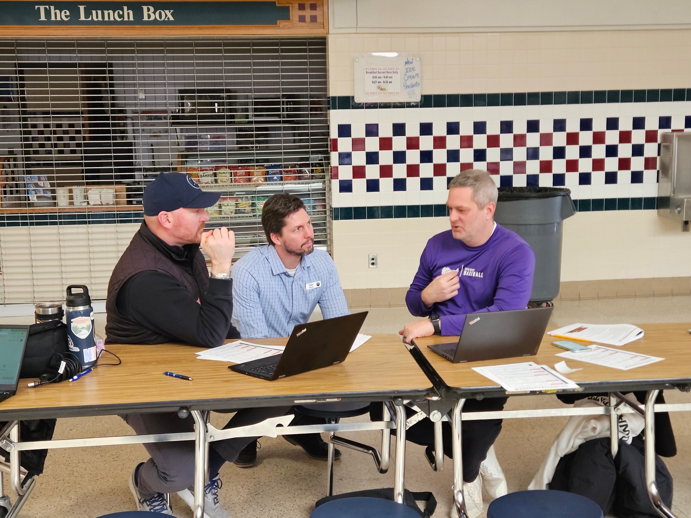Tyler sitting at a cafeteria table with two participants, working through a problem on their laptops.
