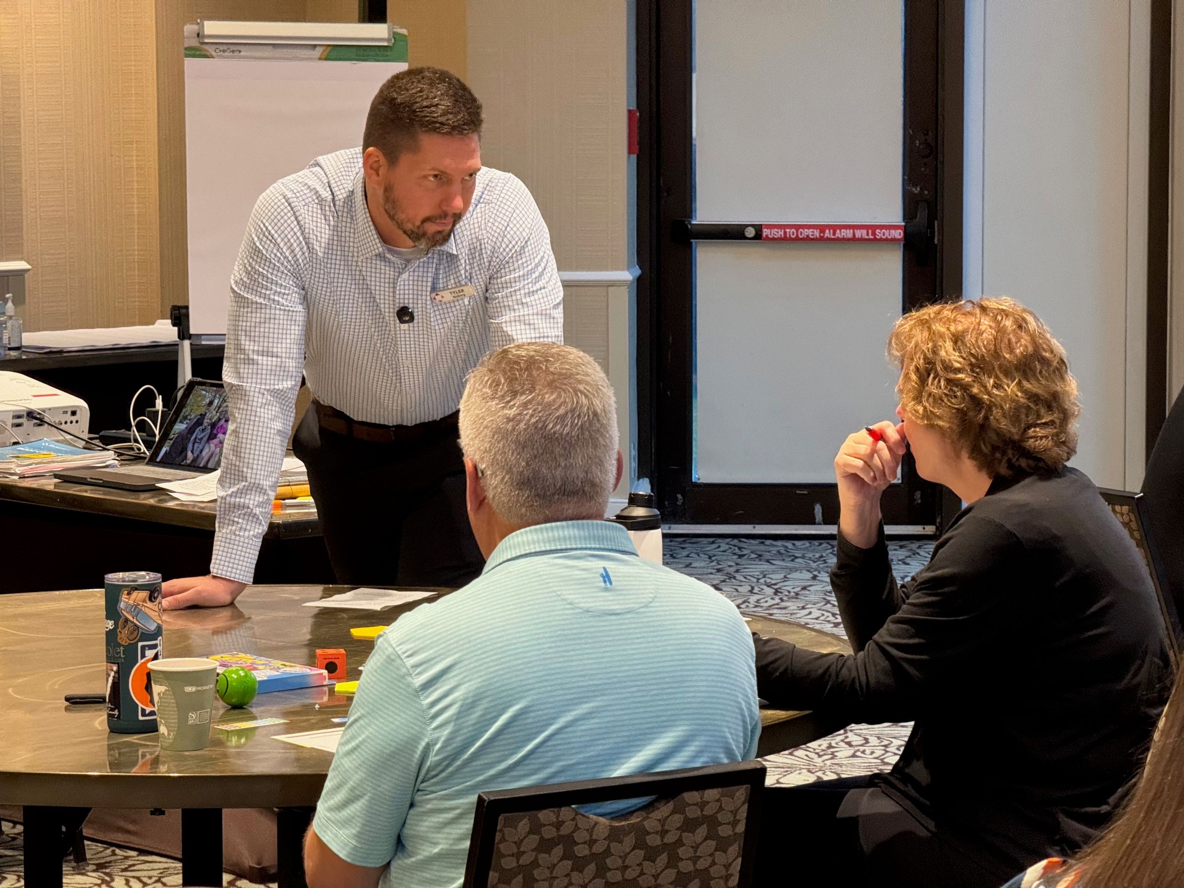 Tyler leaning on a table to talk through an idea with two seated participants.