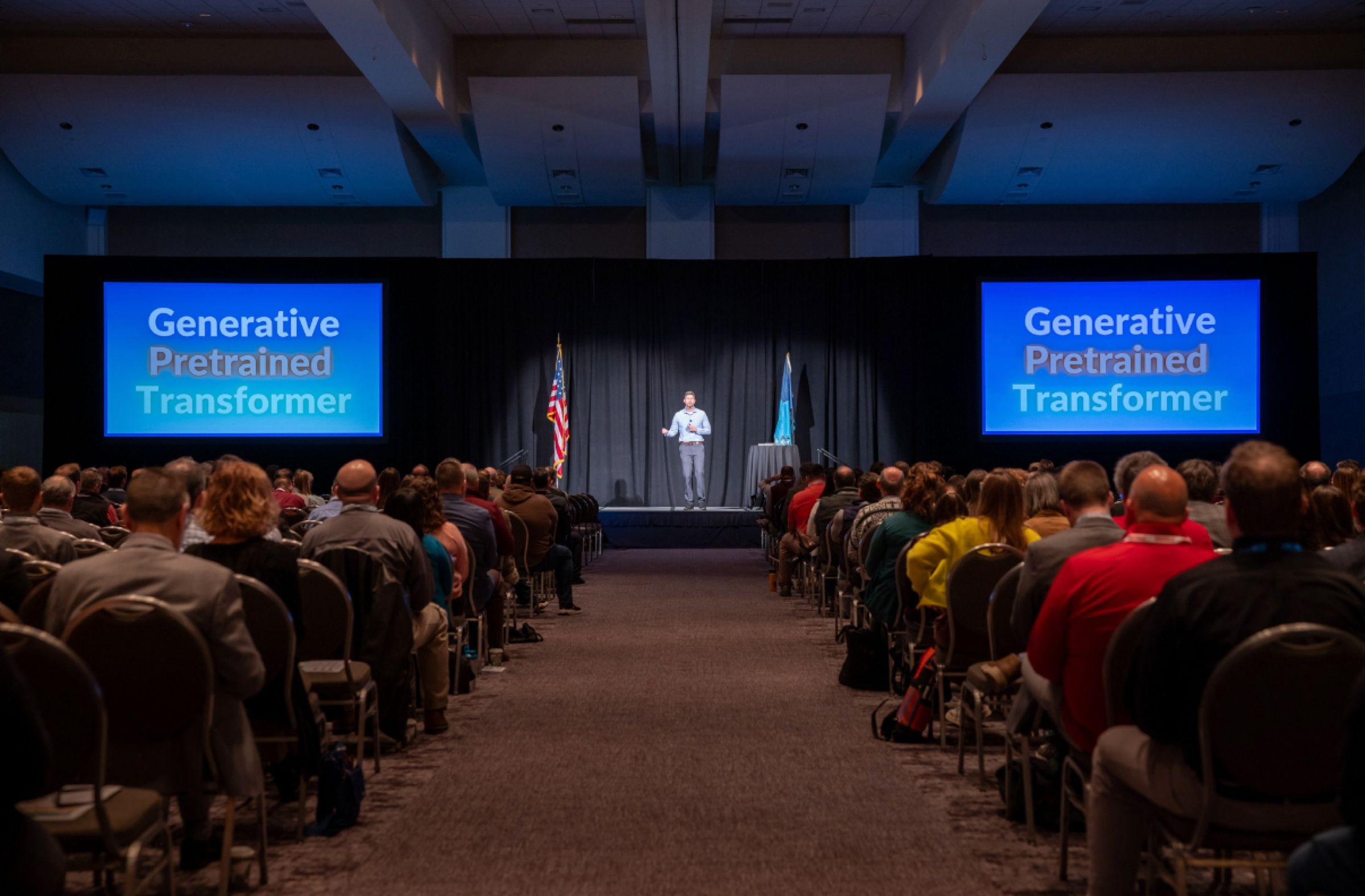Tyler Moberg on a stage between two large screens that read Generative Pretrained Transformer, in front of a packed ballroom audience.
